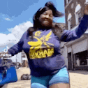 a woman in a purple shirt and blue shorts is dancing on a street .