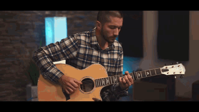 a man in a plaid shirt is playing a guitar