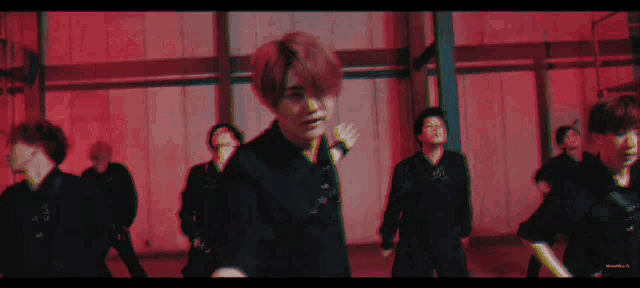 a group of young men are dancing in a dark room with red lights