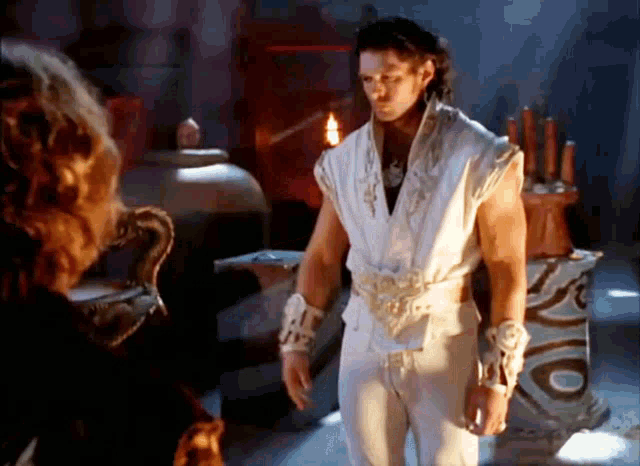 a man in a white outfit is standing in front of a woman in a dark room .