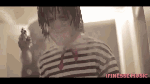 a man in a striped shirt is holding a gun in a bathroom .