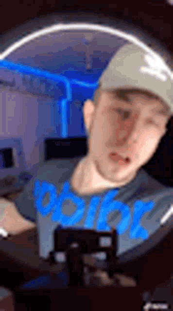 a man wearing a hat and a blue shirt is taking a selfie with a ring light .