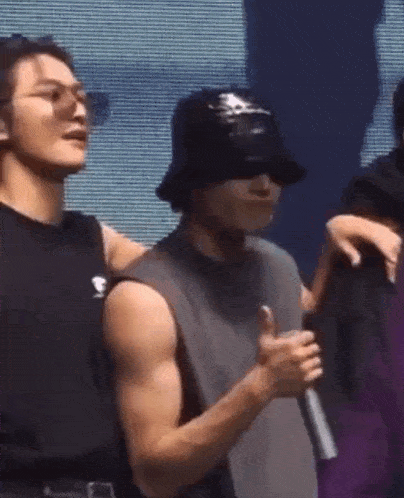 two men are standing next to each other on a stage . one of the men is wearing a bucket hat and sunglasses .