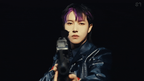 a man with purple hair is holding a gun and looking at the camera