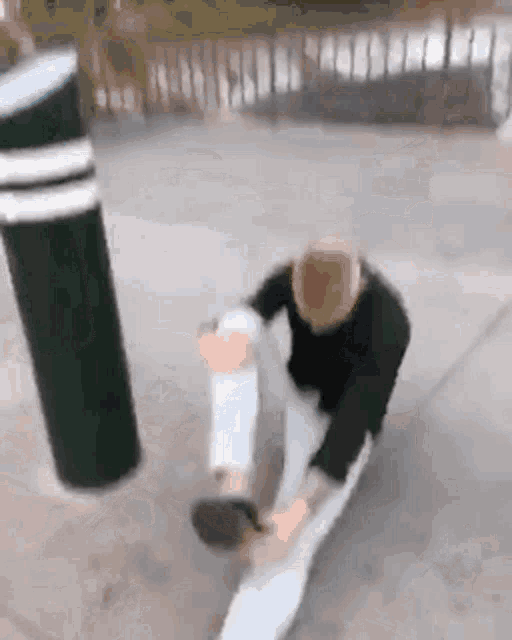 a man is kneeling down on the ground next to a green pole .