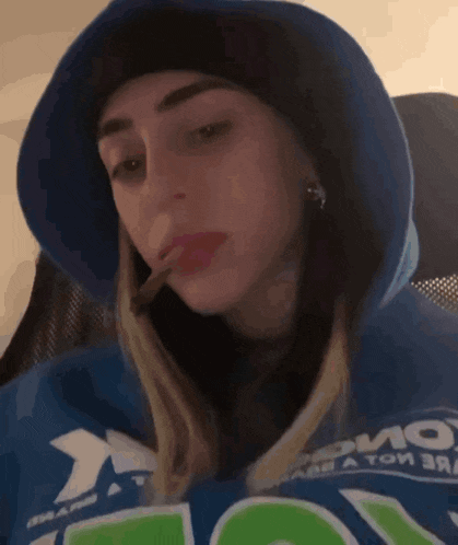 a woman wearing a blue hoodie and a black hat is smoking a cigarette