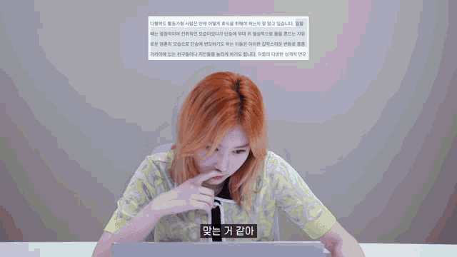 a woman with red hair is sitting in front of a laptop with a foreign language displayed on the screen