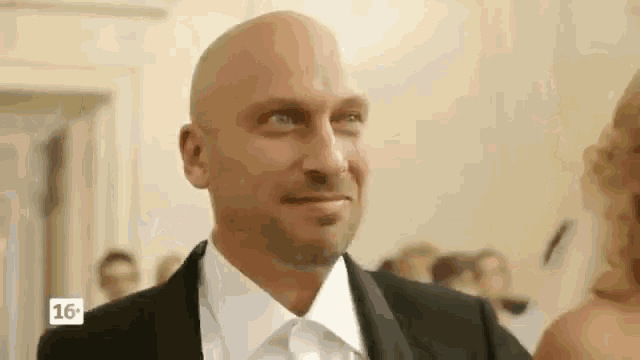 a bald man in a suit and white shirt is smiling while standing next to a woman .
