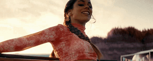 a woman with a braid is sitting in a car with her arms outstretched and smiling .