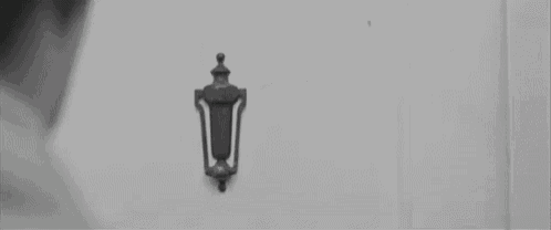 a black and white photo of a woman standing in front of a door with a door knocker on it .
