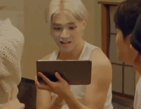 a man in a white tank top is holding a tablet in his hands and laughing .