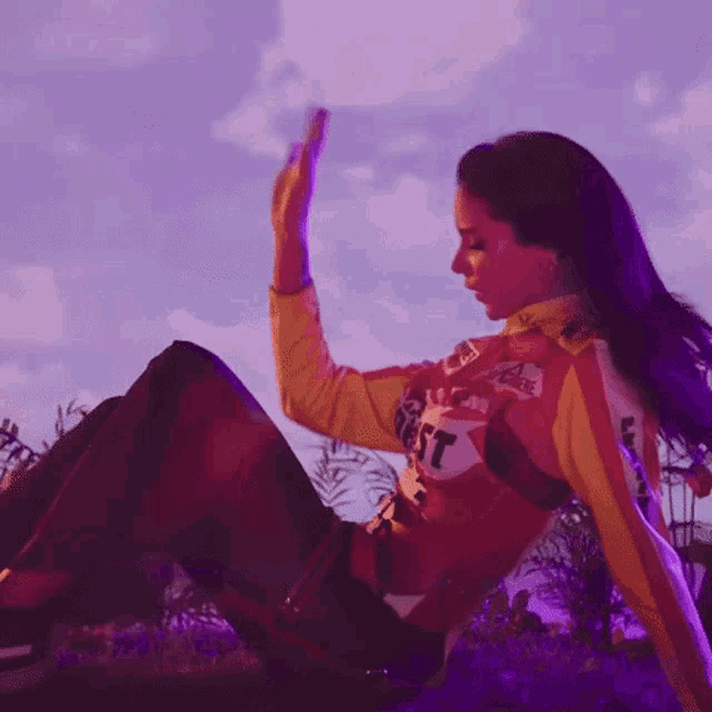 a woman is sitting on the ground in a field with purple lights behind her