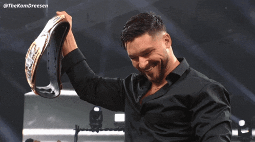 a man wearing a black shirt is holding a wrestling championship belt over his head