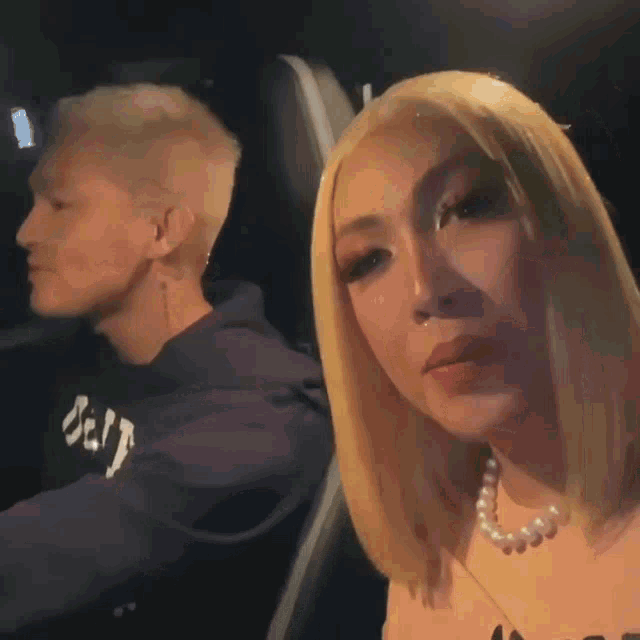 a woman wearing a pearl necklace sits in a car next to a man wearing a hoodie that says jeep