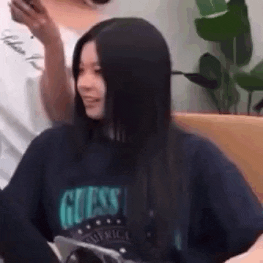 a woman with long black hair is wearing a guess sweatshirt and smiling while sitting on a couch .