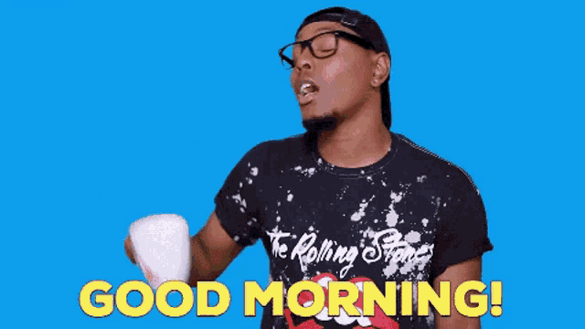 a man in a rolling stones shirt is holding a cup of coffee and says good morning .