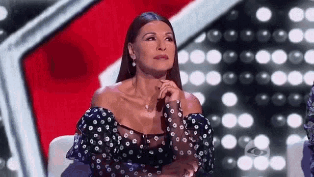 a woman in a black and white polka dot dress is sitting on a stage with her hands on her chin .