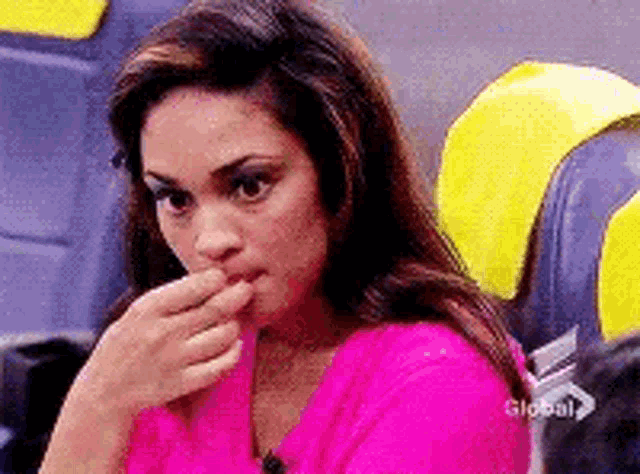 a woman in a pink shirt is sitting in a chair with her hand to her mouth .