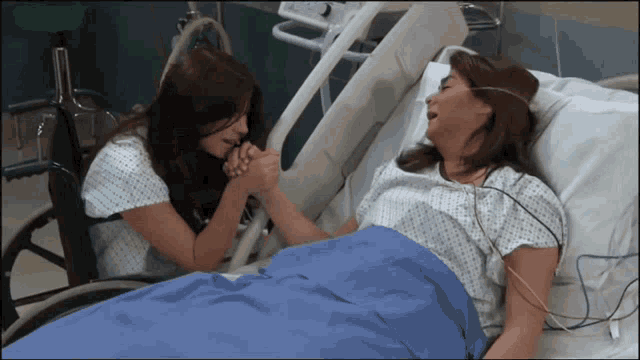 a woman in a hospital bed holds the hand of another woman