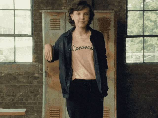a woman wearing a converse t-shirt is standing in front of a locker