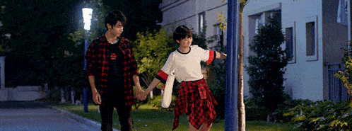 a man and a woman are holding hands while walking down the street .