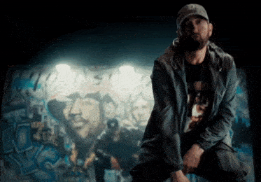 a man kneeling in front of a wall that has graffiti on it and the word eminem on it