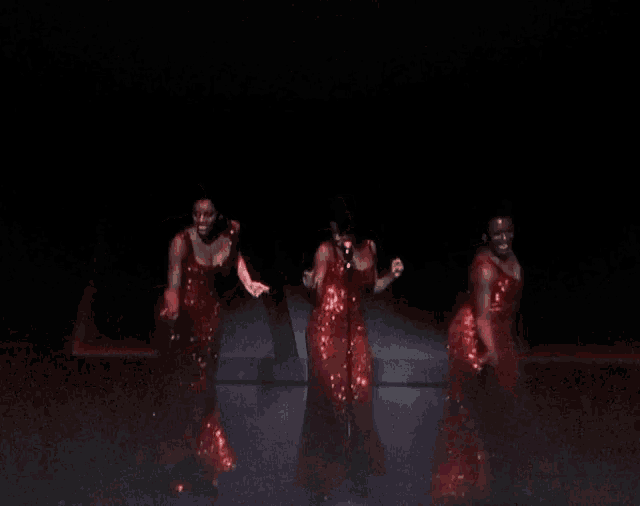 three women in red sequined dresses are dancing and singing on a stage