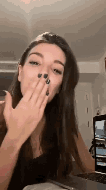 a woman is sitting in front of a laptop computer covering her mouth with her hand .