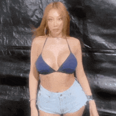a woman in a bikini top and denim shorts is standing in front of a black wall .