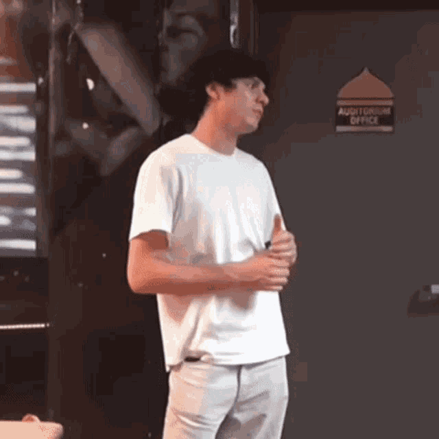 a man in a white t-shirt is standing in front of an auditorium office door .