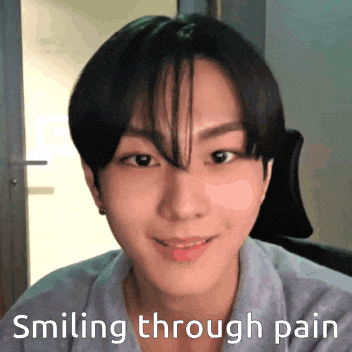 a young man is smiling through pain while wearing a grey shirt