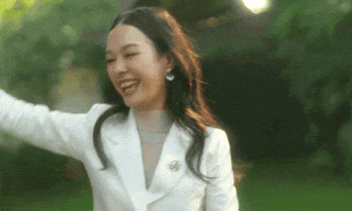 a woman wearing a white jacket and earrings is laughing with her arms outstretched