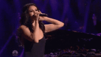 a woman is singing into a microphone on stage .
