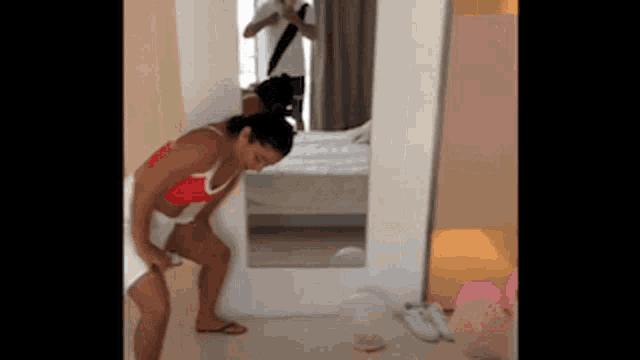 a woman in a red bikini is standing in front of a mirror in a room .