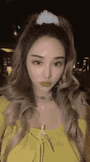a woman wearing a yellow top and a choker with a cross on it