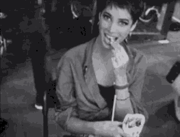 a black and white photo of a woman eating a sandwich with a toothpick .