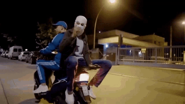 a man in a white mask is riding a motorcycle with another man .