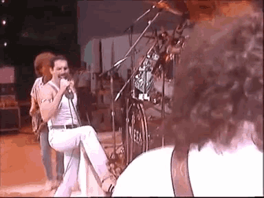 a man singing into a microphone on a stage in front of a drum set