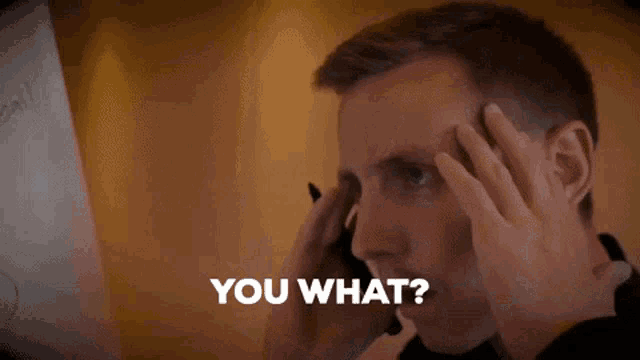 a man is holding his head while talking on a cell phone and says you what .
