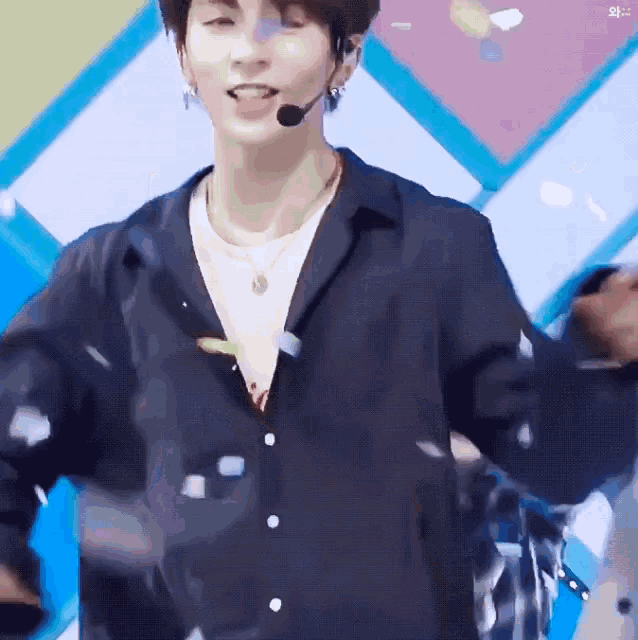 a young man wearing a black shirt and a microphone on his head stands in front of a colorful background