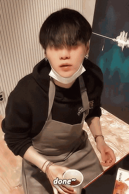 a man wearing an apron and a mask is holding a cup of coffee and says done