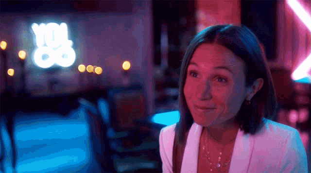 a woman is smiling in front of a neon sign that says " you "