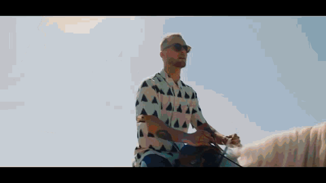 a man wearing sunglasses is riding a horse in the desert