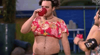 a man is drinking from a red cup while wearing a floral top .