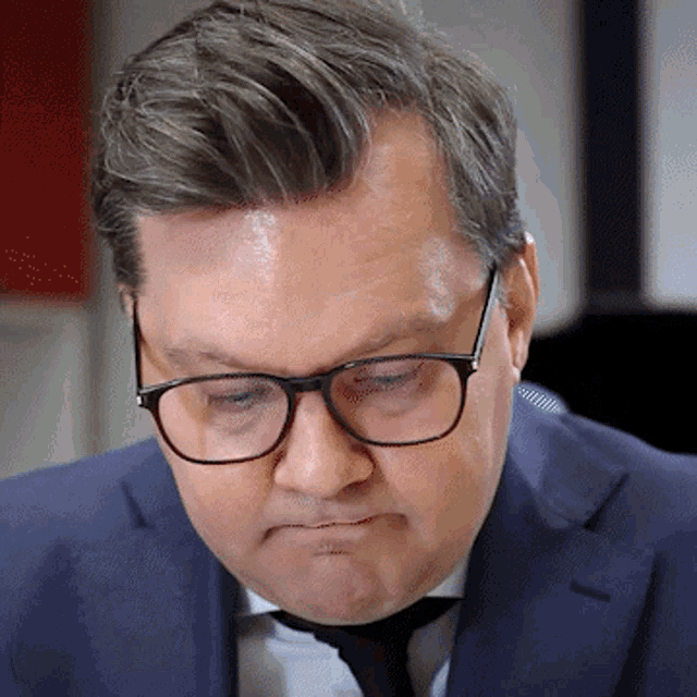 a man wearing glasses and a suit looks down at something