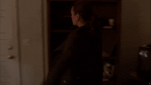 a woman opens a door in a dark room next to a bookshelf with books on it