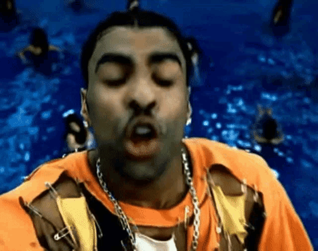 a man in an orange shirt is making a funny face in front of a pool of water .
