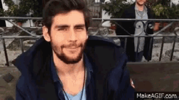 a man with a beard is smiling and looking at the camera while another man stands behind him .