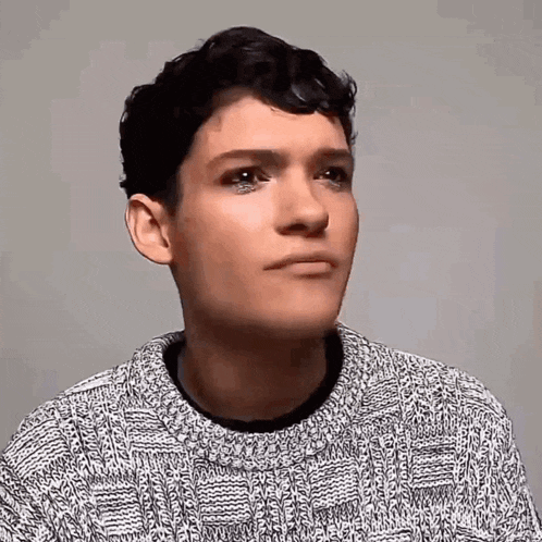 a young man is wearing a sweater and making a funny face .