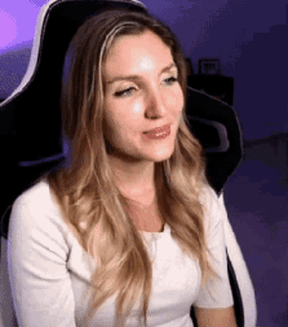 a woman in a white shirt is sitting in a gaming chair looking at the camera .